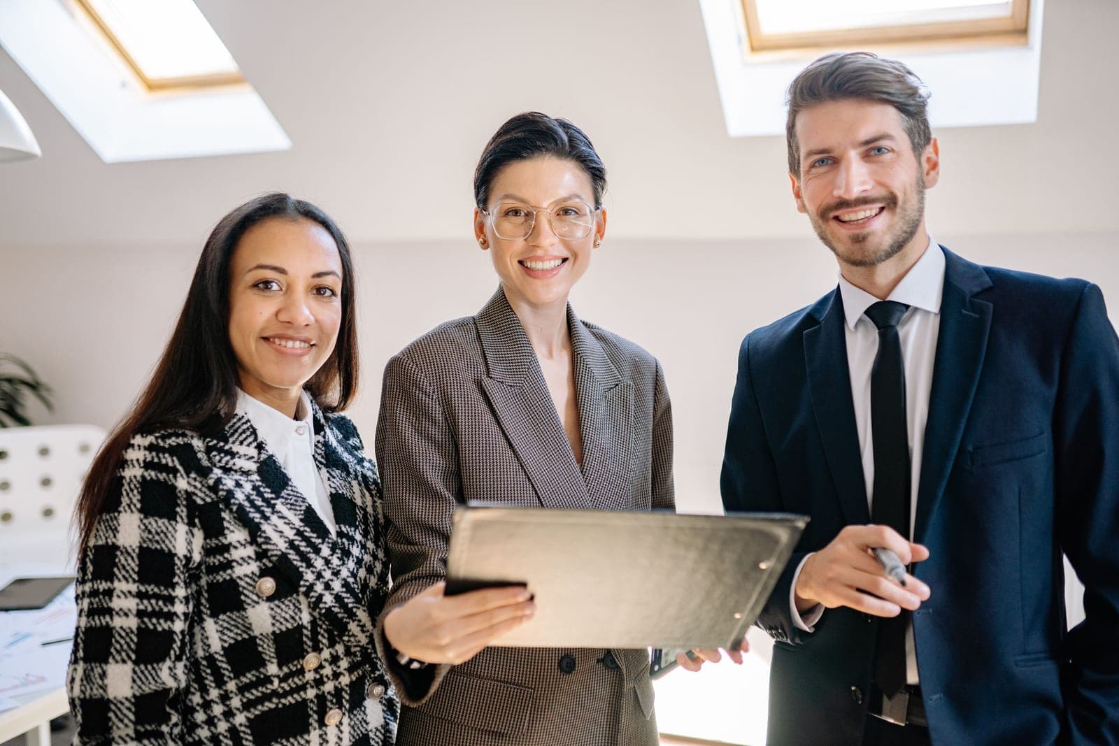 Trois professionnels réunis dans un espace de travail baigné de lumière naturelle, tournés vers l'objectif.